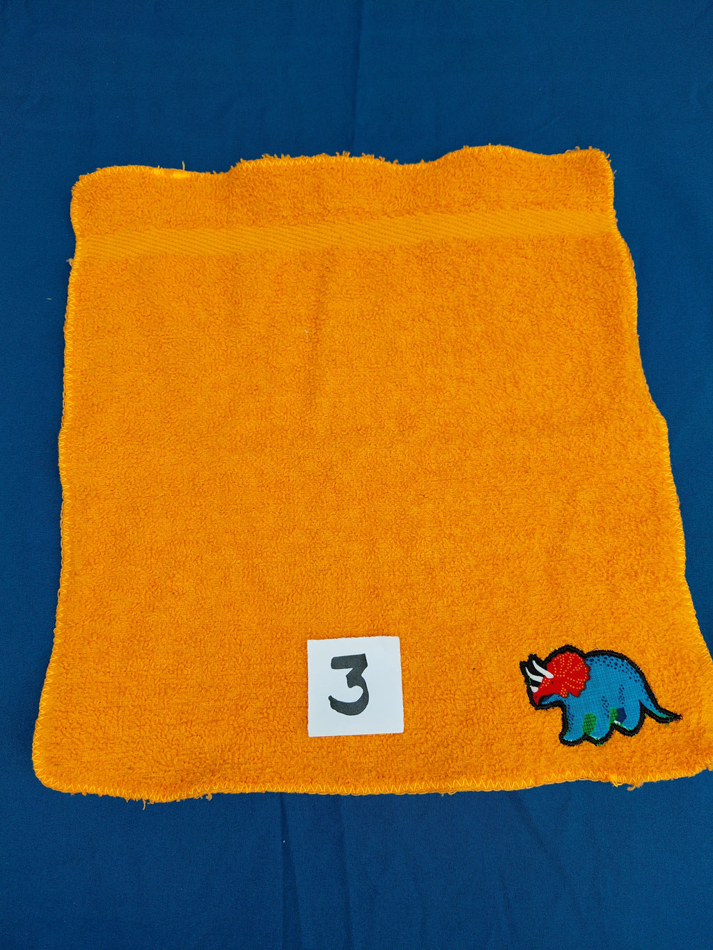 Orange washcloth embellished with a dinosaur design